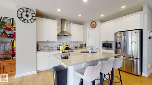 Kitchen featuring white cabinetry, light wood-finish flooring, a center island with a light-toned countertop, and stainless steel appliances - 22407 99 Avenue Nw, Edmonton, AB 