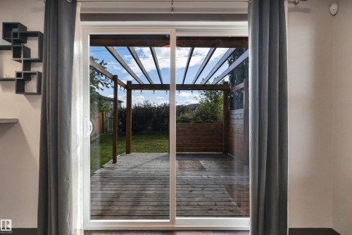 Sliding glass door leading to a wood-finish deck with an overhead pergola, a wood-finish planter box, and a grass lawn - 12903 205 Street Nw, Edmonton, AB 