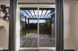 Sliding glass door leading to a wood-finish deck with an overhead pergola, a wood-finish planter box, and a grass lawn - 