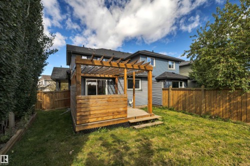 Two-story residence with blue siding, wood pergola, raised wood deck, and a fenced backyard with a large grass area - 12903 205 Street Nw, Edmonton, AB 