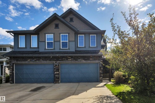 Stone and siding exterior with dual garage doors, concrete driveway, and established landscaping - 12903 205 Street Nw, Edmonton, AB 