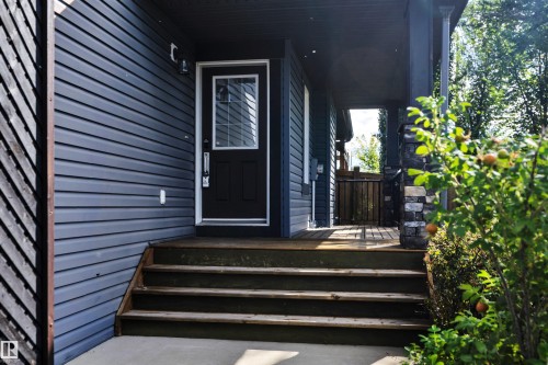 Entryway featuring horizontal siding, a solid entry door with an upper glass panel, a covered porch, and wood stairs - 12903 205 Street Nw, Edmonton, AB 