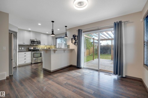 Wood-finish flooring throughout, kitchen with white cabinetry, stainless steel appliances, and a tiled backsplash - 12903 205 Street Nw, Edmonton, AB 