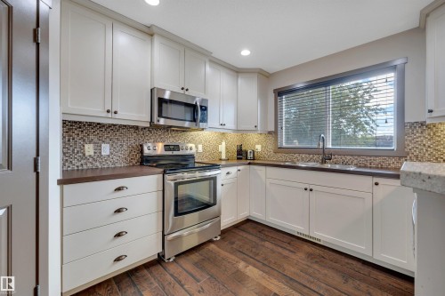 White shaker-style cabinetry, wood-finish flooring, stainless steel appliances, mosaic tile backsplash, and recessed lighting - 12903 205 Street Nw, Edmonton, AB 