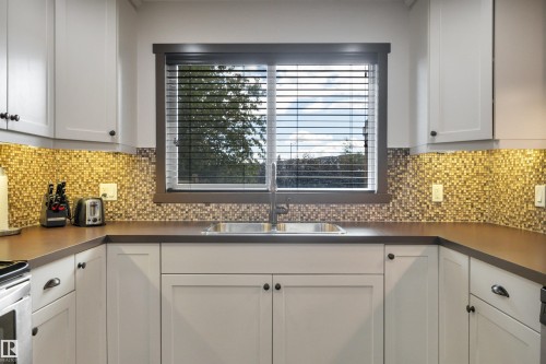 White shaker-style cabinetry with dark hardware, mosaic tile backsplash, composite countertop, and double basin stainless steel sink - 12903 205 Street Nw, Edmonton, AB 