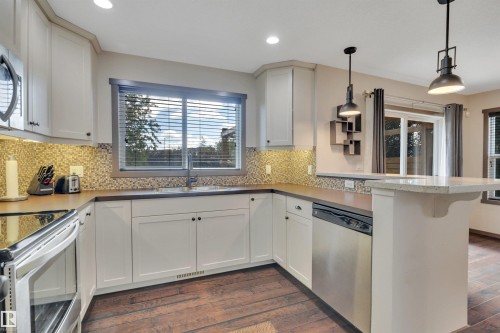 Kitchen featuring white cabinetry, stainless steel appliances, mosaic tile backsplash, wood-finish flooring, and a breakfast bar with pendant lighting - 12903 205 Street Nw, Edmonton, AB 