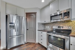 Stainless steel appliance suite, light-toned cabinetry, mosaic tile backsplash, wood-finish flooring, and dark countertops - 