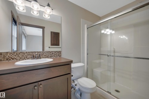Bathroom featuring a wood-finish vanity with an integrated sink, mosaic tile backsplash, and a glass-enclosed shower with a built-in bench - 12903 205 Street Nw, Edmonton, AB 