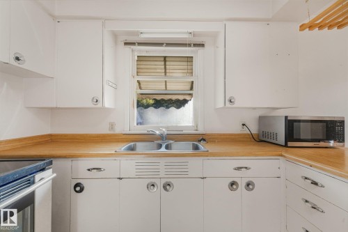 White cabinetry with circular and bar hardware, wood-finish countertops, and a double basin stainless steel sink - 11507 135 Street Nw, Edmonton, AB 
