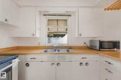 White cabinetry with circular and bar hardware, wood-finish countertops, and a double basin stainless steel sink - 