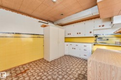 White cabinetry with circular hardware, yellow tile backsplash, wood-look ceiling, patterned floor tile, and a tall built-in storage unit - 