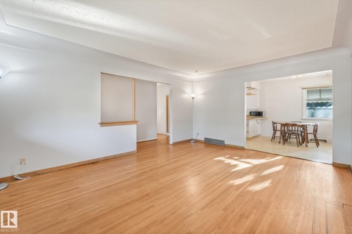 Wood-finish flooring throughout, white painted walls, and an archway leading to a separate area with a window - 11507 135 Street Nw, Edmonton, AB 