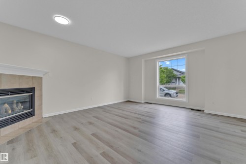Spacious room featuring light wood-finish flooring, a contemporary fireplace with a tile surround, and a large window providing ample natural light - 2912 31 Street Nw, Edmonton, AB 