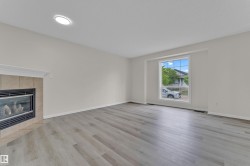 Spacious room featuring light wood-finish flooring, a contemporary fireplace with a tile surround, and a large window providing ample natural light - 