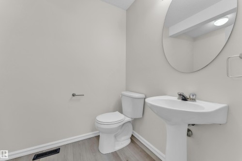 Pedestal sink with chrome faucet, toilet, wall-mounted mirror, and wood-finish flooring - 2912 31 Street Nw, Edmonton, AB 