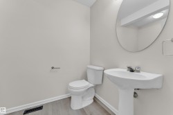Pedestal sink with chrome faucet, toilet, wall-mounted mirror, and wood-finish flooring - 
