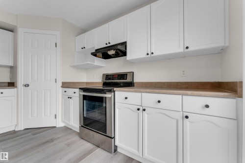 Kitchen featuring white cabinetry, light wood-finish flooring, stainless steel range, and brown countertops - 2912 31 Street Nw, Edmonton, AB 