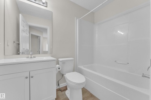 White vanity with cabinet storage, chrome faucet, rectangular mirror, and an integrated bathtub with shower - 2912 31 Street Nw, Edmonton, AB 