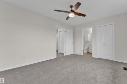 Neutral wall paint with gray carpeting, featuring a ceiling fan with light fixture, white interior doors, and a double-door closet - 