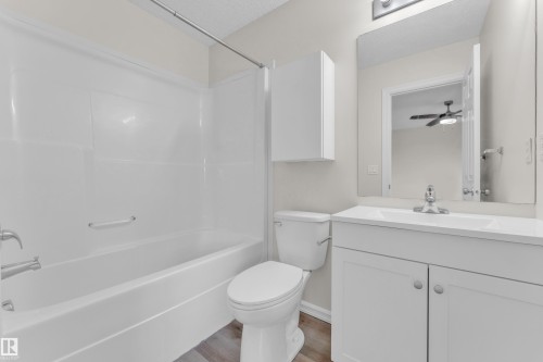 Tub/shower combination with grab bar, white vanity with integrated sink, wall-mounted mirror, and wood-finish flooring - 2912 31 Street Nw, Edmonton, AB 