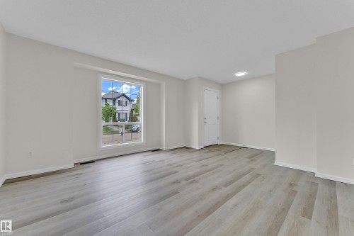 Spacious room featuring wood-finish flooring, ample natural light from a large window, a white entry door, and a recessed ceiling light - 2912 31 Street Nw, Edmonton, AB 