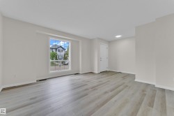 Spacious room featuring wood-finish flooring, ample natural light from a large window, a white entry door, and a recessed ceiling light - 