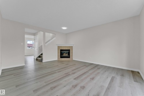Expansive living area with wood-finish flooring, a tiled fireplace with mantel, recessed lighting, and a staircase with carpeted treads - 2912 31 Street Nw, Edmonton, AB 