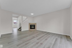 Expansive living area with wood-finish flooring, a tiled fireplace with mantel, recessed lighting, and a staircase with carpeted treads - 