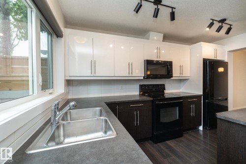Modern kitchen featuring white upper cabinetry, dark lower cabinetry, dark countertops, and coordinating black appliances - 53/55 Michigan Street, Devon, AB 