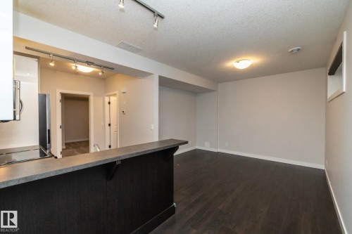 Open concept living space featuring dark wood-finish flooring, a breakfast bar with a dark wood-finish base and light-colored countertop, track lighting, and a modern ceiling light fixture - 53/55 Michigan Street, Devon, AB 