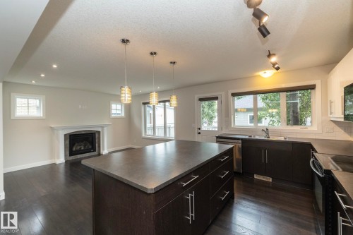 Open-concept living area featuring dark wood-finish flooring, a built-in fireplace with a white mantel, and recessed lighting - 53/55 Michigan Street, Devon, AB 