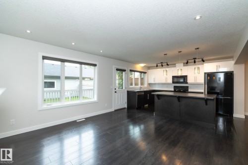 Kitchen featuring a central island, black appliances, white and dark cabinetry, and pendant lighting - 53/55 Michigan Street, Devon, AB 
