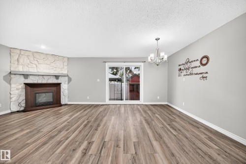 Wood-finish flooring throughout, complemented by a stone-clad fireplace with a wood mantel - 18146 81 Avenue Nw, Edmonton, AB 