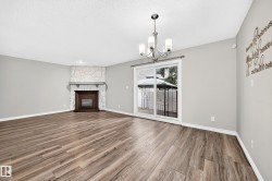 Wood-finish flooring throughout, stone-clad fireplace with wood surround, sliding glass door access to exterior, and a contemporary chandelier - 