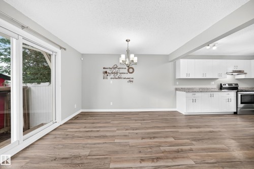 Wood-finish flooring, white cabinetry, integrated stainless steel appliances, granite-look countertops, and a sliding glass door - 18146 81 Avenue Nw, Edmonton, AB 