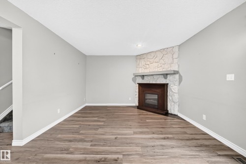 Corner fireplace with a stone surround, wood-finish flooring, and light gray wall finishes - 18146 81 Avenue Nw, Edmonton, AB 