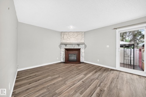 Wood-finish flooring, stone-clad fireplace with wood surround, recessed lighting, and sliding glass door to exterior - 18146 81 Avenue Nw, Edmonton, AB 