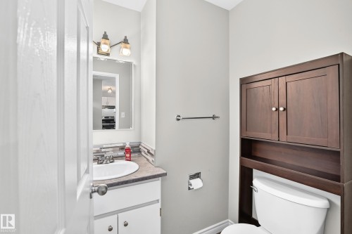 Vanity with integrated sink, modern backsplash, wall-mounted lighting, and wood-finish storage cabinetry - 18146 81 Avenue Nw, Edmonton, AB 
