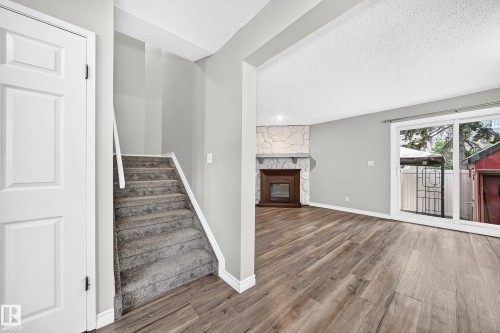 Living space featuring a stone-clad fireplace, wood-finish flooring, and sliding glass doors - 18146 81 Avenue Nw, Edmonton, AB 