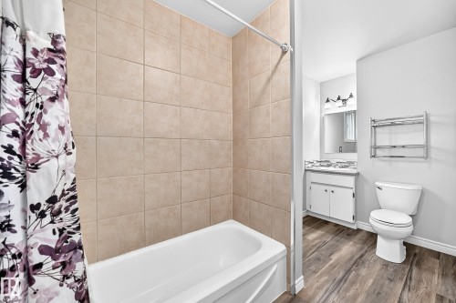 Bathroom featuring a tiled shower surround, white bathtub, wood-finish flooring, and a vanity with a mirrored medicine cabinet - 18146 81 Avenue Nw, Edmonton, AB 