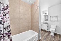Bathroom featuring a tiled shower surround, white bathtub, wood-finish flooring, and a vanity with a mirrored medicine cabinet - 