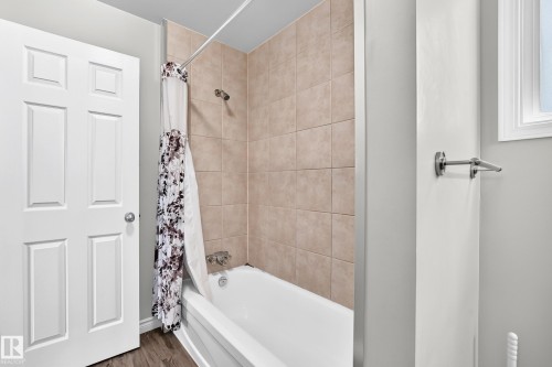 Bathtub shower combination with tiled surround, wood-finish flooring, and white interior door - 18146 81 Avenue Nw, Edmonton, AB 