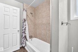 Bathtub shower combination with tiled surround, wood-finish flooring, and white interior door - 