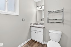 Bathroom with wood-finish flooring, a white vanity with an undermount sink, mosaic tile backsplash, and a three-light vanity fixture - 