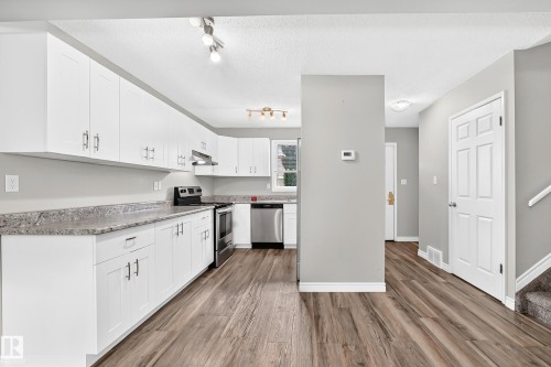 Kitchen featuring white cabinetry, stone-finish countertops, stainless steel appliances, and wood-finish flooring - 18146 81 Avenue Nw, Edmonton, AB 