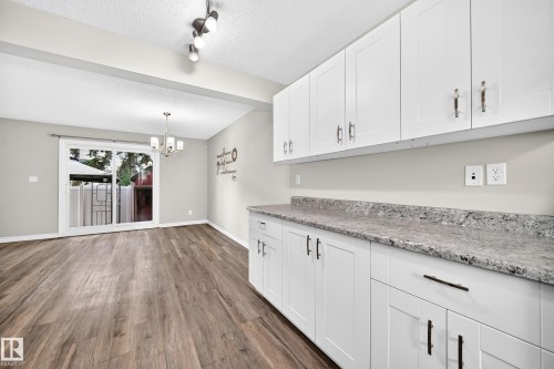 White shaker-style cabinetry with dark hardware, speckled countertops, wood-finish flooring, and a sliding glass door - 18146 81 Avenue Nw, Edmonton, AB 