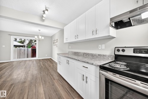 White cabinetry with stainless hardware, stone-finish countertops, wood-finish flooring, and a sliding glass door to the exterior - 18146 81 Avenue Nw, Edmonton, AB 