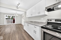 White cabinetry with stainless hardware, stone-finish countertops, wood-finish flooring, and a sliding glass door to the exterior - 