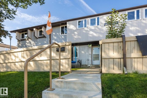 Concrete walkway leading to the entrance, front door with storm door, wooden fence enclosing a private outdoor area, and a light-colored exterior finish - #2 14120 80 St Nw, Edmonton, AB 