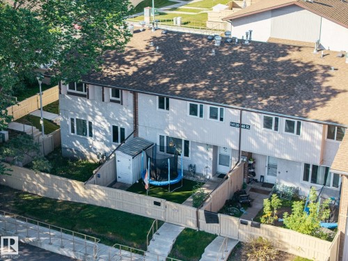 Townhome exterior with two levels, a shingled roof, individual fenced yards, and a street sign indicating location - #2 14120 80 St Nw, Edmonton, AB 